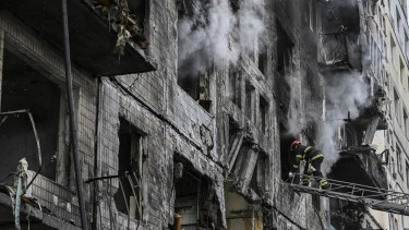 Un bombero en una escalera ingresa a un edificio de departamentos en llamas después de que fue bombardeado hoy en Kiev. Foto AFP